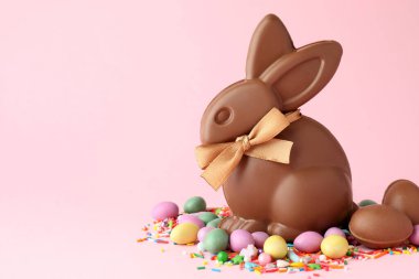 Çikolatalı Paskalya tavşanı, yumurtalar, şekerler ve pembe arka plana serpiştirilmiş şekerler. Metin için boşluk