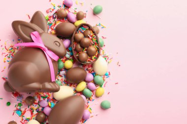 Çikolatalı Paskalya tavşanı, yumurtalar, şekerler ve pembe arka plana serpiştirilmiş şekerler, düz yatak. Metin için boşluk