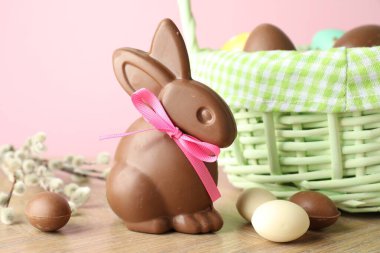 Çikolatalı Paskalya tavşanı ve hasır sepetteki yumurtalar ahşap masada pembe arka planda, yakın plan.