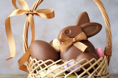 Çikolatalı Paskalya tavşanı ve hasır sepette yumurtalar açık gri arka planda, yakın plan.