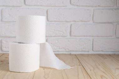 Beyaz tuğla duvarın yanındaki ahşap masada tuvalet kağıdı ruloları, yakın plan. Metin için boşluk