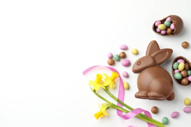 Çikolatalı Paskalya tavşanı, çiçekler, beyaz arka planda kurdele ve yumurtalar, düz yatak. Metin için boşluk