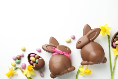 Beyaz arka planda çikolatalı Paskalya tavşanları, çiçekler, kurdele ve yumurtalar, düz yatak. Metin için boşluk