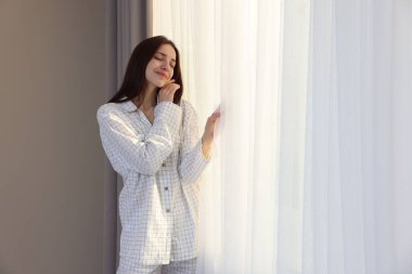 Pencerenin yanında güzel perdeleri olan mutlu bir kadın.