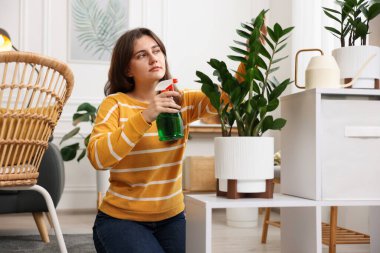 Bir kadın güzel saksı bitkisini suyla ıslatıyor.