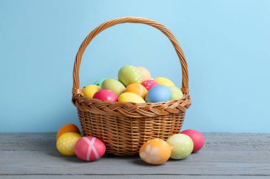 Hasır sepetin içine boyanmış Paskalya yumurtaları açık mavi arka plana karşı gri ahşap masa üzerinde