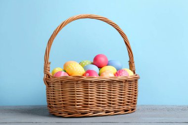 Hasır sepetin içine boyanmış Paskalya yumurtaları açık mavi arka plana karşı gri ahşap masa üzerinde