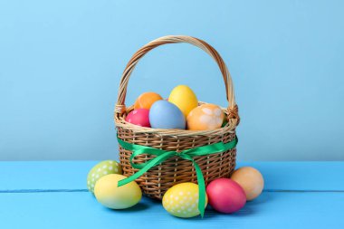 Hasır sepetin içine boyanmış Paskalya yumurtaları açık mavi arka plana karşı ahşap masada.