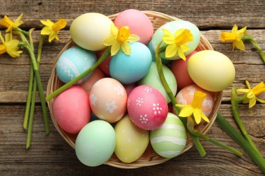 Hasır sepete boyanmış Paskalya yumurtaları ve ahşap masaya serilmiş güzel nergisler.