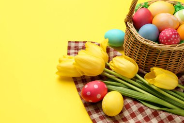 Sarı arka planda boyanmış yumurtalar ve laleler olan Paskalya sepeti, yakın plan. Metin için boşluk