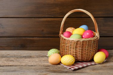 Tahta masadaki hasır sepete boyanmış Paskalya yumurtaları. Metin için boşluk