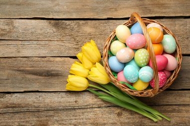 Tahta masanın üzerinde boyanmış yumurtalar ve laleler olan Paskalya sepeti. Metin için boşluk