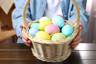 Paskalya sepetinde boyanmış yumurtalı bir kadın, kapalı masa, yakın plan.