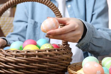 Paskalya sepetinde yumurta boyalı bir kadın, kapalı bir masada, yakın plan.