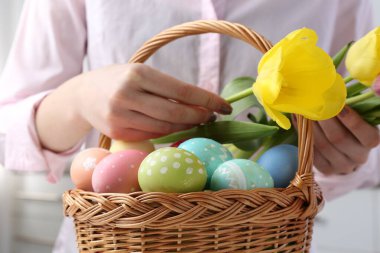 Paskalya sepetinde yumurta boyalı bir kadın ve kapalı bir masada laleler, yakın plan.