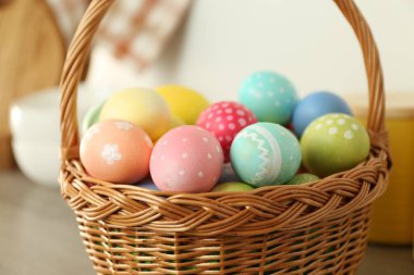 Kapalı alandaki ahşap masada boyanmış yumurtaların olduğu Paskalya sepeti, yakın plan.