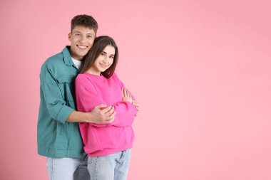 Mutlu çift pembe arka planda birbirine sarılıyor, mesaj için yer var.