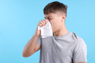 Açık mavi arka planda burnu akan genç bir adam, mesaj için yer var. Soğuk Semptom