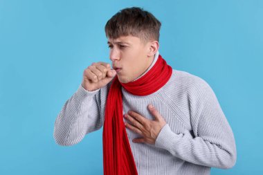 Açık mavi arka planda öksüren hasta genç bir adam. Soğuk Semptom
