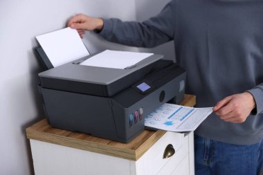 Kapalı alandaki gri duvarın yanındaki çekmecelerin yanındaki yazıcıdan baskı kağıdı alan adam.