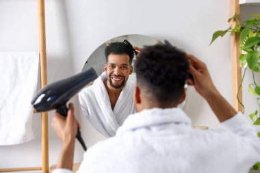 Adam banyoda aynanın yanında saçını kurutuyor.