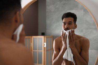 Yakışıklı adam banyoda aynanın yanında yüzünü havluyla siliyor.