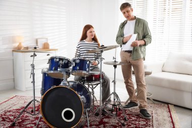 Genç kız içeride müzik öğretmeniyle bateri çalmayı öğreniyor.