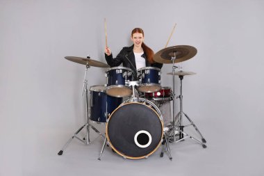 Açık gri arka planda bagetleri ve davulları olan genç bir kız.