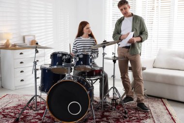 Genç kız içeride müzik öğretmeniyle bateri çalmayı öğreniyor.