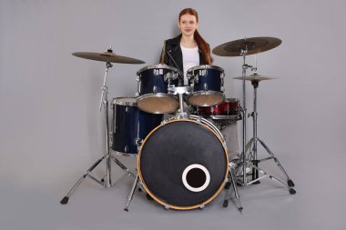 Açık gri arka planda bagetleri ve davulları olan genç bir kız.