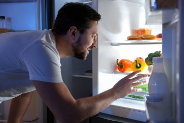 Adam mutfaktaki açık buzdolabına bakıyor.