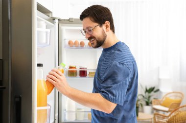 Adam mutfaktaki açık buzdolabından portakal suyu alıyor.