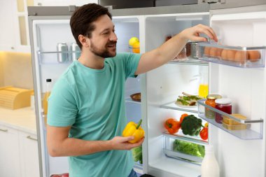 Dolapta dolmalık biberli bir adam buzdolabından yumurta çıkarıyor.