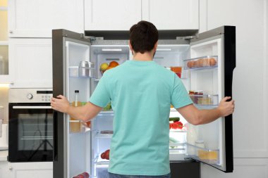 Buzdolabının yanında farklı gıda ürünleri olan bir adam var.