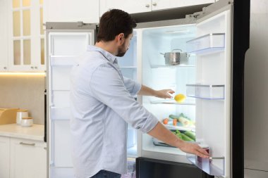 Adam mutfaktaki buzdolabından limon alıyor.