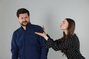 Utangaç adam açık gri arka planda bir kadından öpüşmeyi reddediyor.