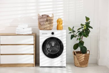 Çamaşır sepetinde kirli havlu ve çamaşır makinesinin üzerinde deterjan var.