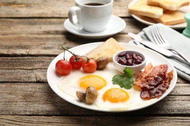 Geleneksel İngiliz kahvaltısı. Lezzetli, güneşli tarafı domuz pastırmalı, kırmızı fasulyeli, domatesli, mantarlı ve ahşap masada servis edilen kızarmış ekmekli yumurtalar.