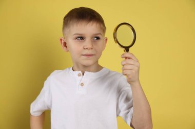 Sarı arka planda büyüteç olan küçük çocuk.