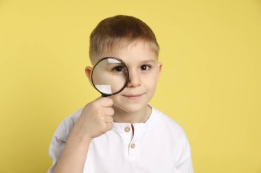 Sarı arka planda büyüteç olan küçük çocuk.