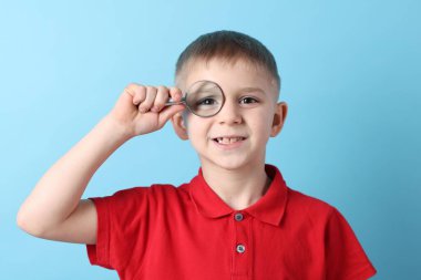 Açık mavi arka planda büyüteç takan küçük çocuk.