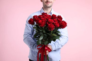 Sevgililer Günü kutlaması. Pembe arka planda güzel kırmızı gül buketi olan adam, yakın plan.