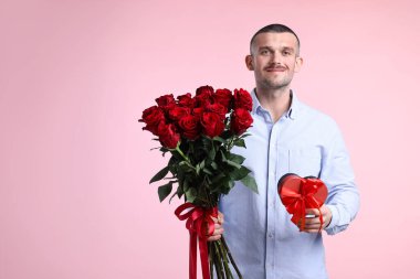 Sevgililer Günü kutlaması. Güzel bir buket kırmızı gül ve pembe arka planda hediye kutusu olan bir adam.