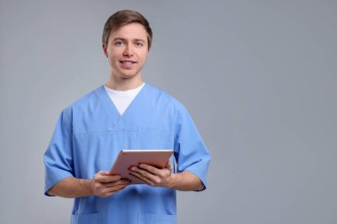 Gri arkaplan üzerinde tableti olan tıbbi asistanın portresi, metin için boşluk