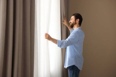 Evde şık pencere perdeleri açan adam