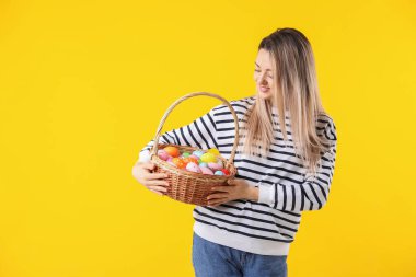 Paskalya kutlaması. Sarı arka planda boyanmış yumurta dolu sepeti olan gülümseyen kadın, mesaj için yer.