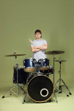 Beyzbol şapkalı, davul setiyle yeşil arka planda genç bir çocuk.