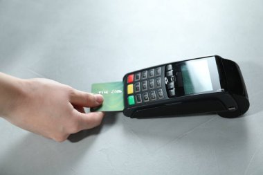 Kredi kartı olan bir kadın beyaz masada ödeme terminalini kullanıyor.