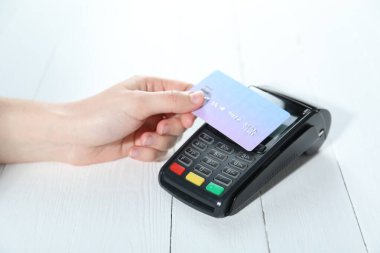Kredi kartı olan bir kadın beyaz tahta masada ödeme terminalini kullanıyor, yakın plan.