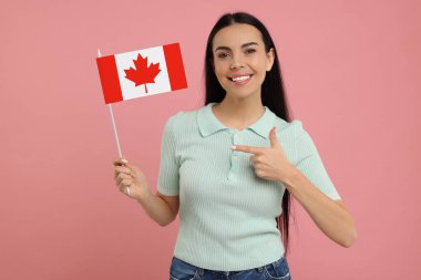 Mutlu kadın pembe arka planda elinde Kanada bayrağını gösteriyor.